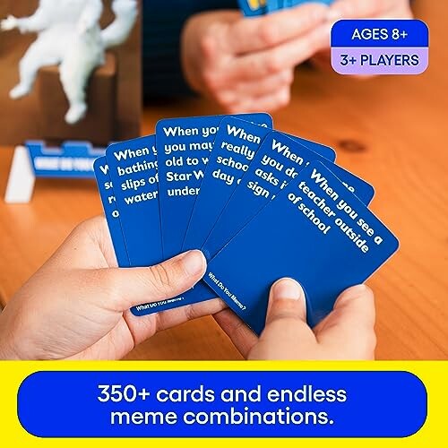 Hands holding blue cards from a meme card game, suitable for ages 8 and up.